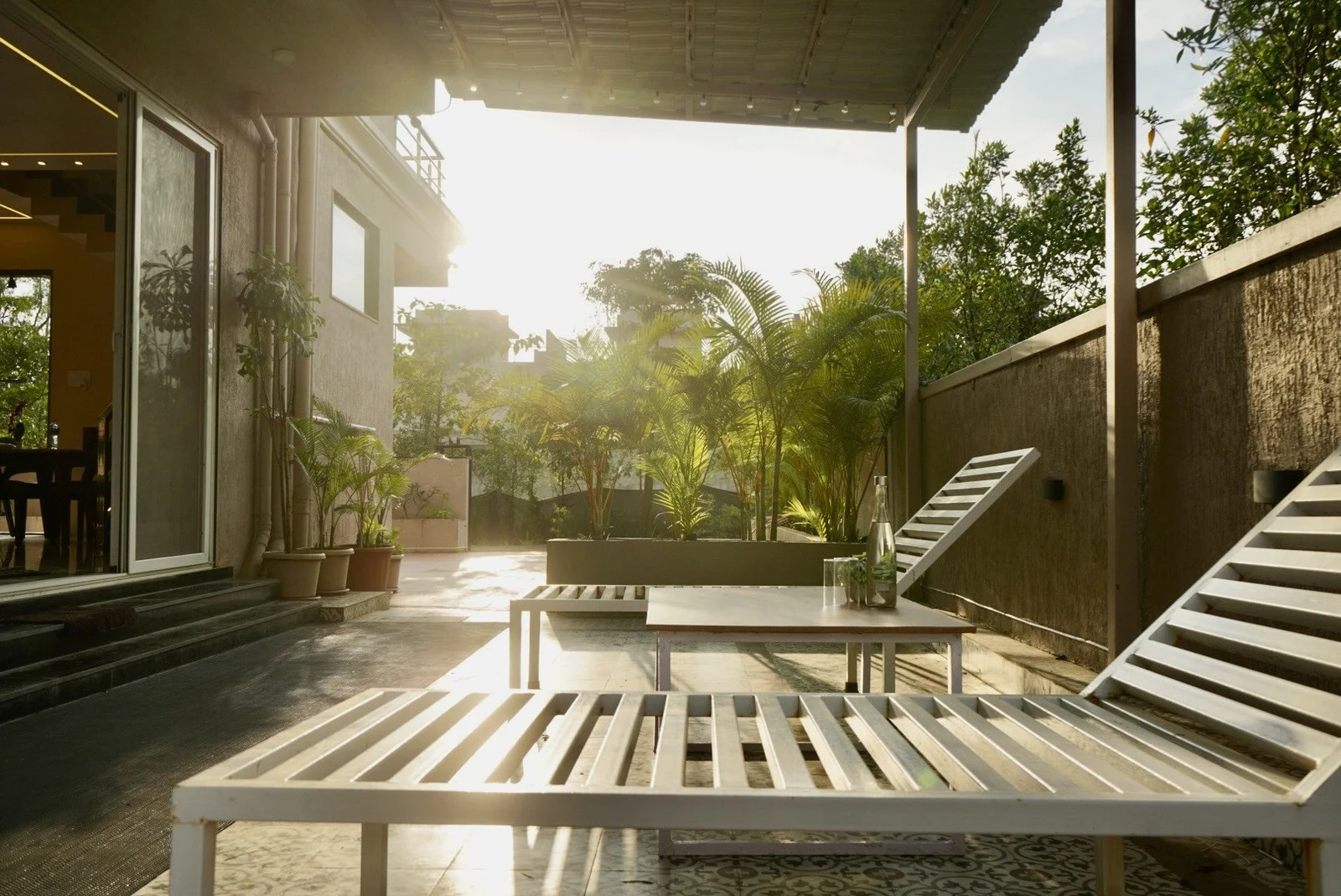 White loungers on a shaded deck, with morning sunlight coming through the palms beside the villa.
